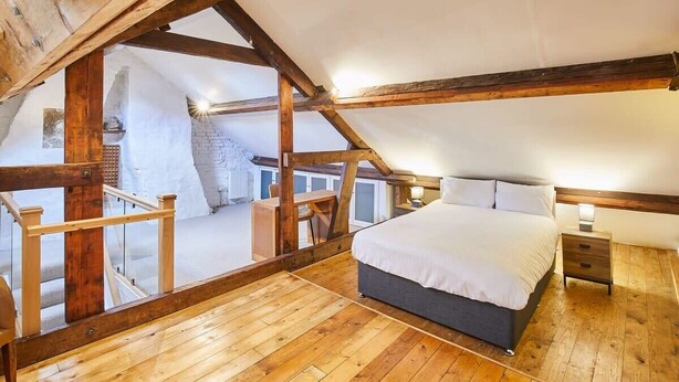 A bedroom with a wooden ceiling and exposed beams, a bed, a nightstand, and a view of a balcony. - Host & Stay | The Duck Pond (Durham)