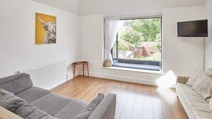 A modern living room with a grey sofa, a beige sofa, a large window with curtains, a flat-screen TV, and a painting of a bull. - Host & Stay | The Duck Pond (Durham)