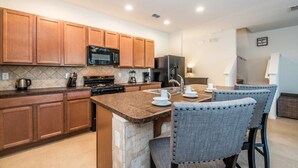 A modern kitchen with wooden cabinets, a granite countertop, and a central island with bar stools. - Amazing 4br Resort Townhome W/ Splash Pool-4686td 4 Bedroom Villa by RedAwning (Davenport)