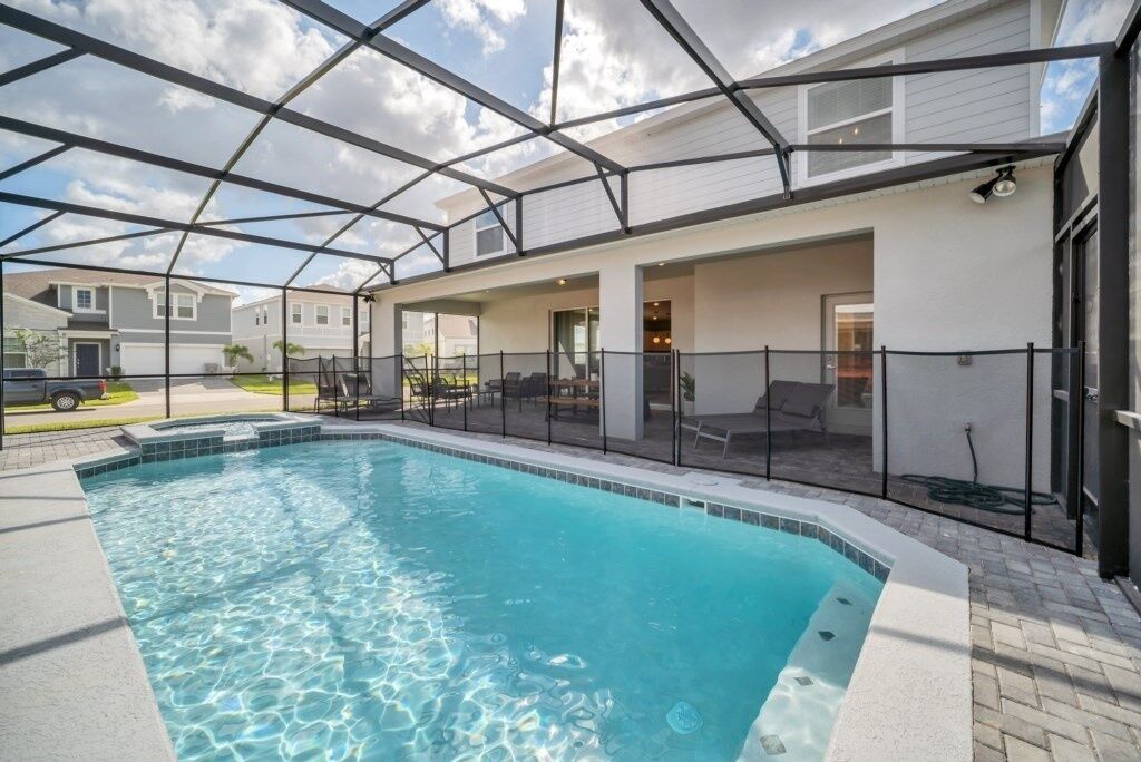 Une piscine dotée d’une structure en verre, entourée d’un patio aménagé avec des sièges d’extérieur.