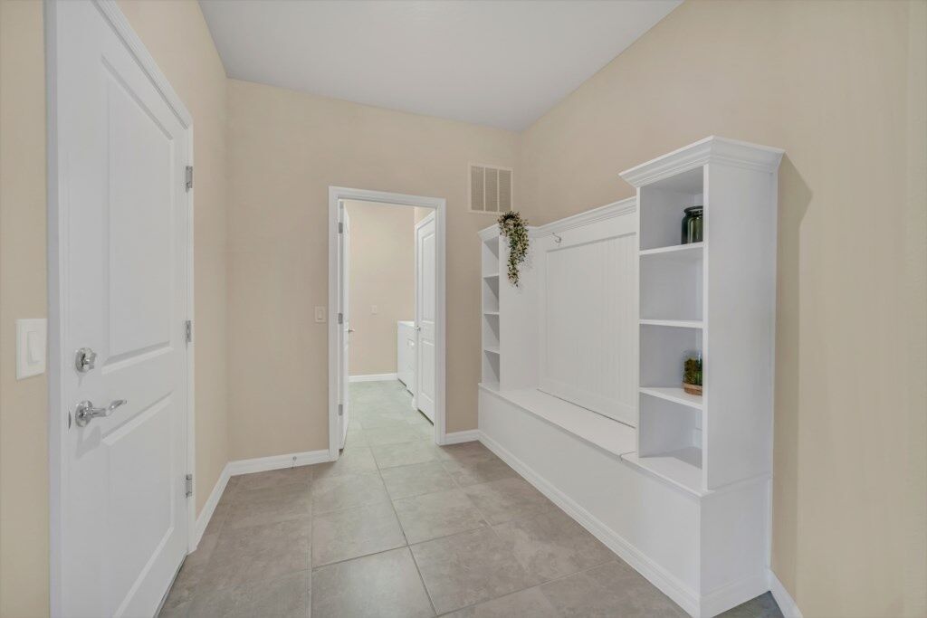 Een gang met beige muren en witte deuren, die leidt naar een kamer met een wit inbouwplanksysteem.