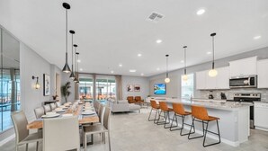 Une cuisine moderne dotée d’un îlot central, de tabourets de bar et d’un coin repas avec une longue table et des chaises.