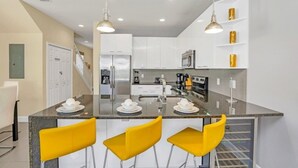 A modern kitchen with white cabinets, stainless steel appliances, and a central island with yellow bar stools. - 1511retreat 3 Bedroom Townhouse by Redawning (Clermont)