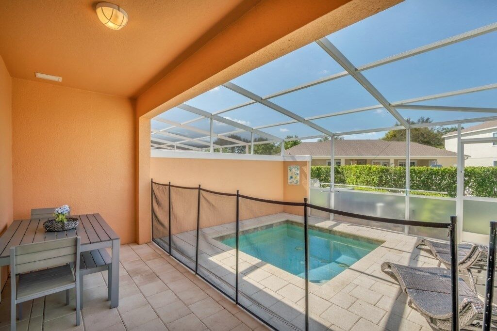 Un espace extérieur abrité avec une piscine, une table entourée de chaises et, au loin, une maison.
