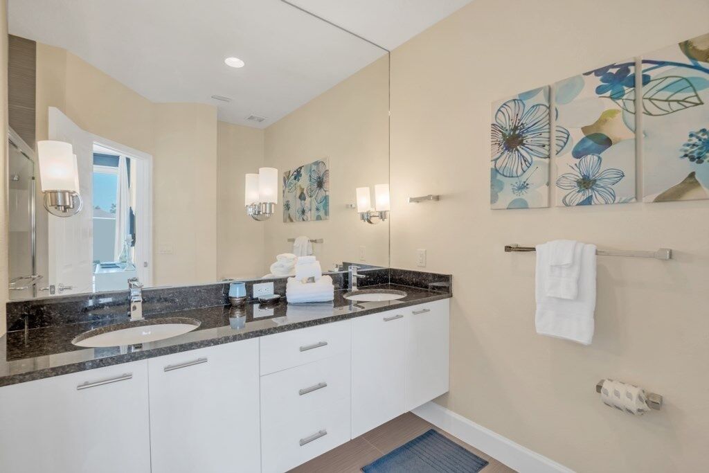A modern bathroom with two sinks, a large mirror, wall-mounted lights, and a towel rack.