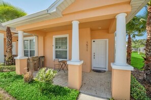 A building with a peach-colored exterior, white columns, a door labeled "151", and a small patio area with a table and chairs. - 1511retreat 3 Bedroom Townhouse by Redawning (Clermont)