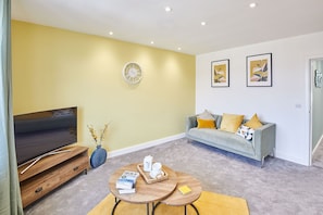 A living room with a sofa, a coffee table, a TV, and artwork on the wall.