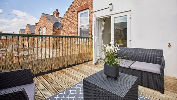 A balcony with wicker furniture, a wooden fence, and a brick building in the background. - Host & Stay | Morgan's Rest (Scarborough)