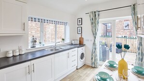 A modern kitchen with white cabinets, a washing machine, and a dining area with teal plates and glasses. - Host & Stay | Morgan's Rest (Scarborough)