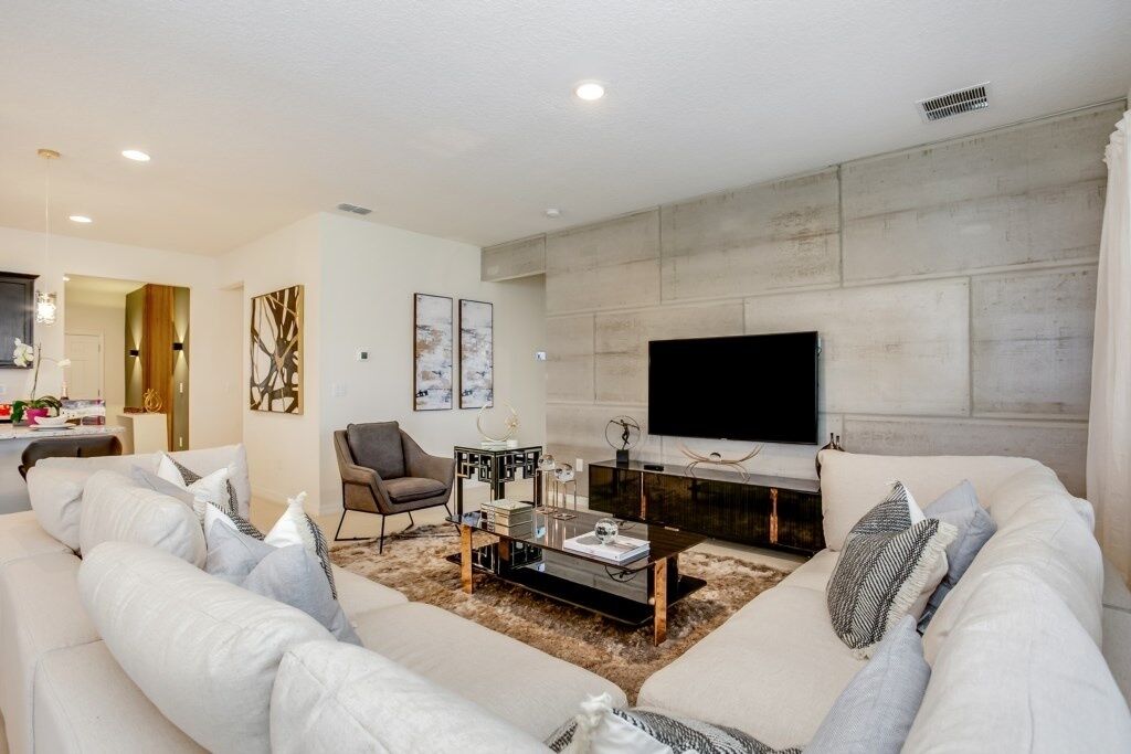 A modern living room with a large sofa, a coffee table, and a flat-screen TV mounted on a stone wall.