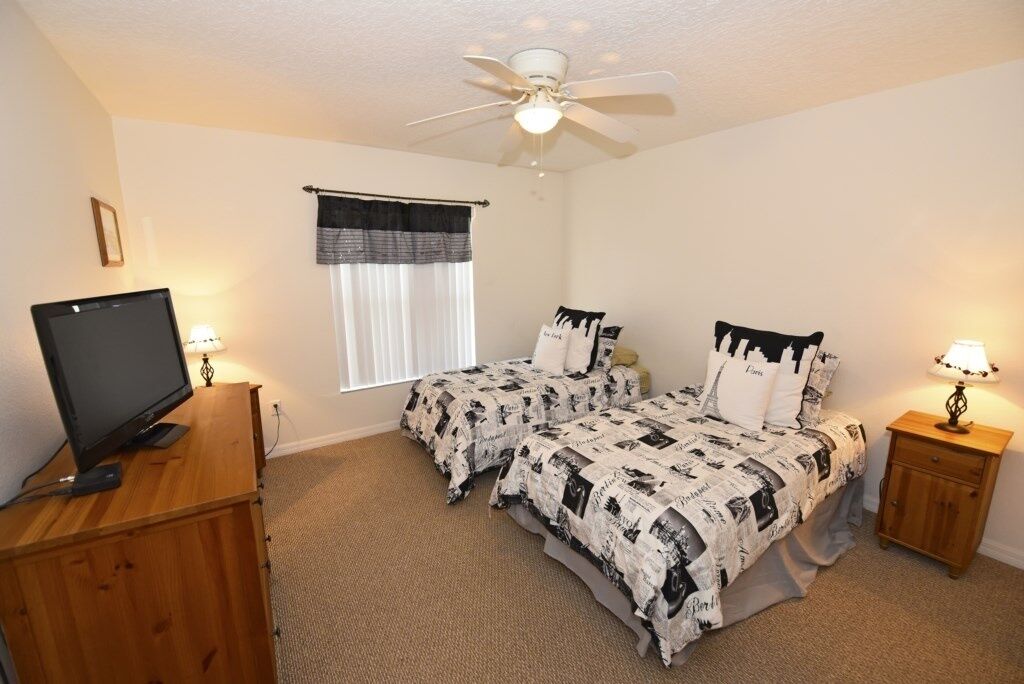 A bedroom with two beds, a ceiling fan, a television on a wooden dresser, and a window with curtains.