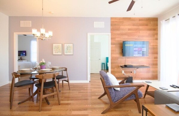 A modern living room with a dining area, wooden flooring, and a mounted flat-screen TV.