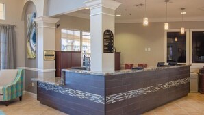 Un espace d’accueil doté d’un comptoir recouvert de carreaux sombres, d’un panneau indiquant les services proposés et donnant sur le hall d’entrée.
