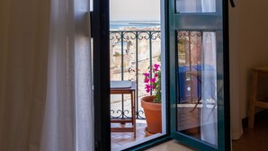 Una habitación con puerta corrediza de vidrio que da a un balcón con planta en maceta y una silla.