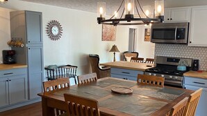 Een eetgedeelte met een houten tafel en stoelen, een kroonluchter, en een keuken met moderne apparatuur.