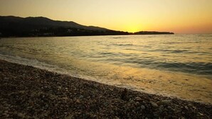 A pebbled beach with a sunset over the water and distant hills.