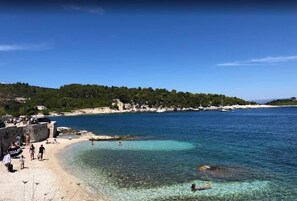 A beach with clear water, people, and a stone wall.