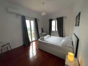 Un dormitorio con cama, mesita de noche, lámpara y vistas al exterior.