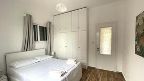 A bedroom with a bed, a wardrobe, a window with curtains, and a door with a patterned glass panel.