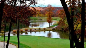 A golf course with a pond, surrounded by trees with autumn foliage.