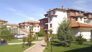A residential area with multiple apartment buildings, a paved pathway, and small trees. - Stunning Apartment With Pool in Ravda, Bulgaria (Nessebar)
