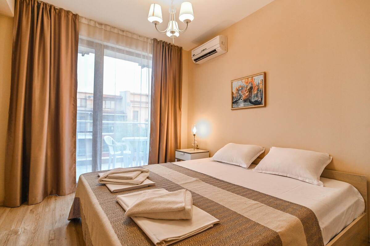 A hotel room with a large bed, a nightstand, a lamp, and a painting on the wall.