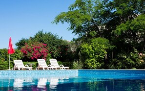 A clear blue pool with white lounge chairs and a red umbrella, surrounded by lush greenery and trees. - Apart-Hotel Onegin (Sozopol)