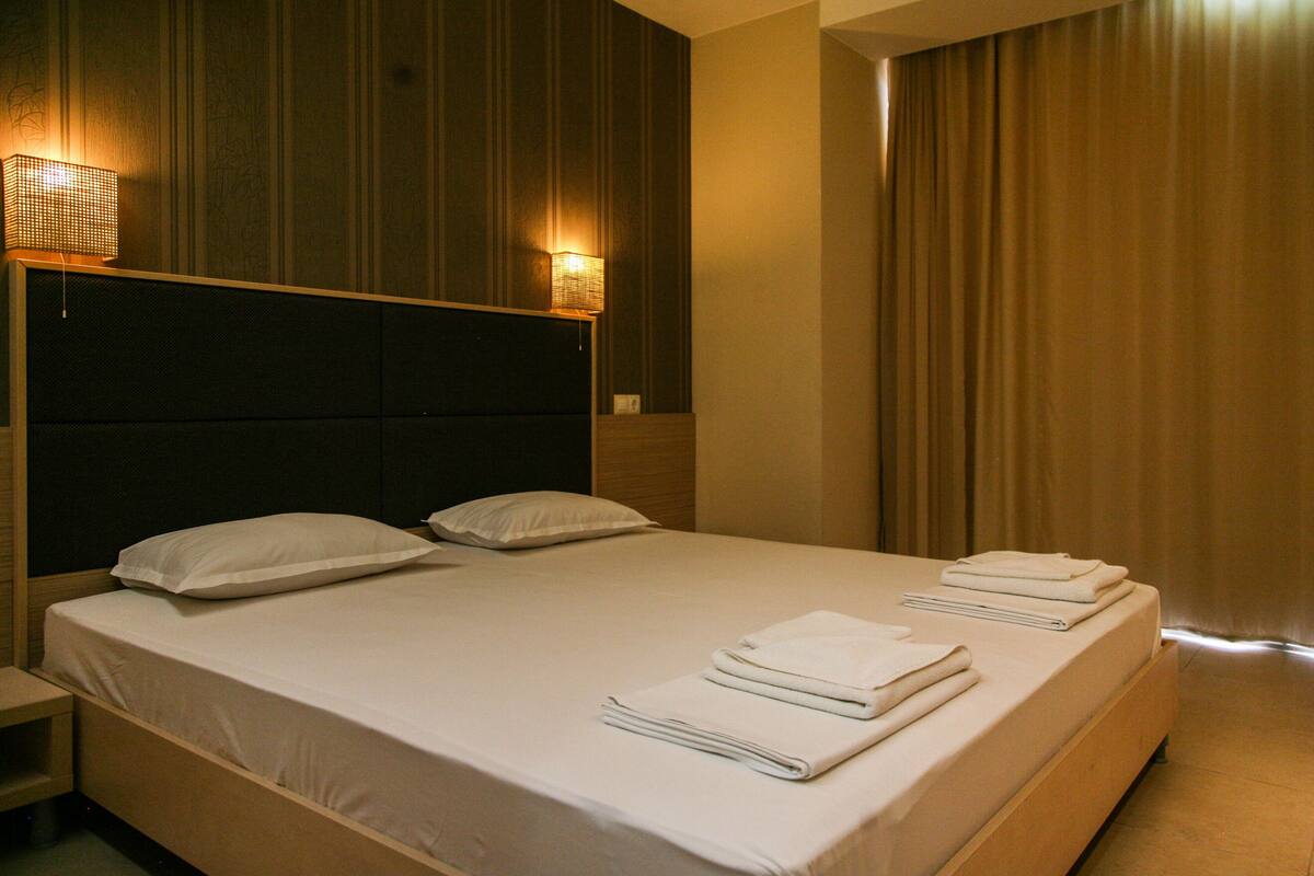 A hotel room with a large bed, two bedside lamps, and neatly folded towels on the bed.