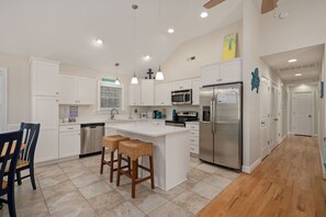Une cuisine moderne avec des meubles blancs, des appareils en acier inoxydable et un îlot central doté de tabourets de bar.