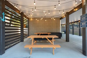 Un espace extérieur aménagé avec des tables de pique-nique en bois et des guirlandes lumineuses.