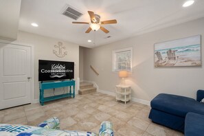 A living room with a television, a ceiling fan, a staircase, and a beach-themed painting. - GaGa's Getaway: Quiet location, dog-Friendly, fire pit, 3-night min. (Kill Devil Hills)