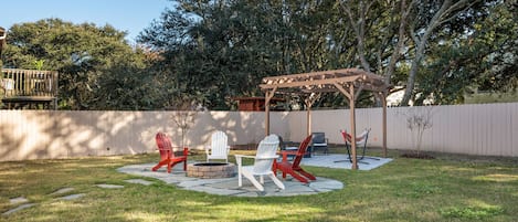 A backyard with a wooden pergola, outdoor seating with Adirondack chairs, and a fire pit.