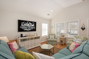 A cozy living room with teal sofas, a patterned armchair, and a flat-screen TV mounted on the wall. - GaGa's Getaway: Quiet location, dog-Friendly, fire pit, 3-night min. (Kill Devil Hills)