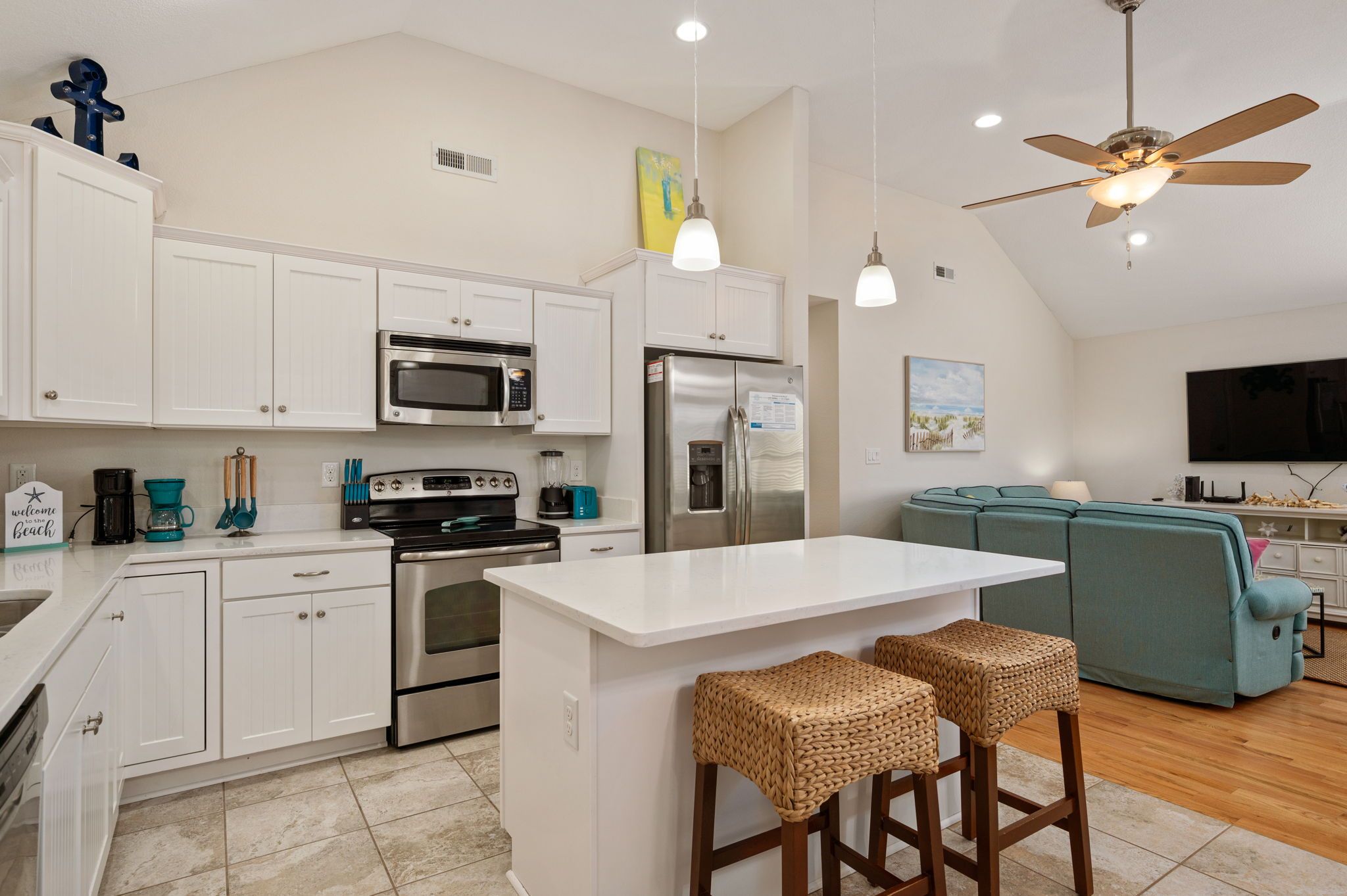 A modern kitchen with white cabinetry, a central island, and a dining area with a teal sofa and bar stools.