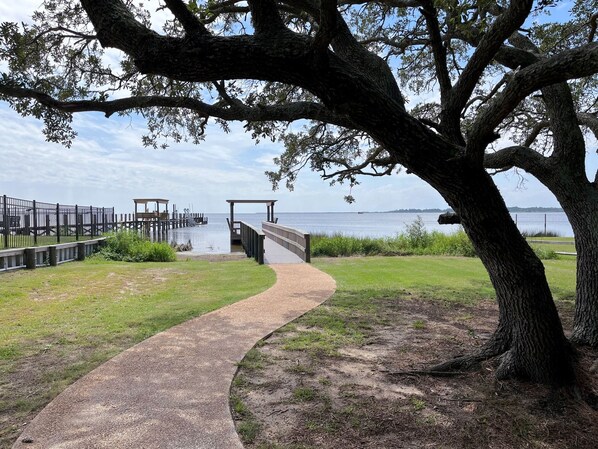 A pathway leading to a wooden dock over water, surrounded by grass and trees. - GaGa's Getaway: Quiet location, dog-Friendly, fire pit, 3-night min. (Kill Devil Hills)