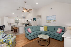 A modern living room with a teal sectional sofa, a small coffee table, and a kitchen area in the background.