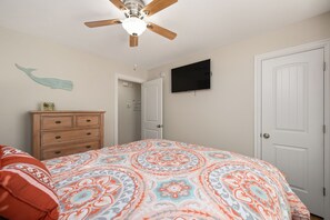 Une chambre à coucher avec un lit, une commode, un ventilateur de plafond, un téléviseur et une porte.