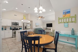 A modern kitchen with white cabinets, a central island, and a dining area with a round table and chairs.