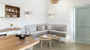 A modern kitchen with a wooden countertop, a built-in shelf with dishes, and a seating area with a grey sofa and two round wooden tables. - Santo Bloom Luxury Villas with Sea View & Two Pools (Santorini)