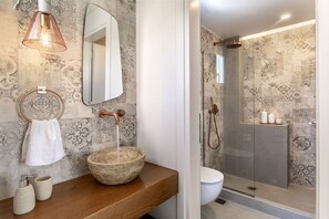 A bathroom with a wooden vanity, a large mirror, a towel ring, a soap dispenser, and a decorative bowl.