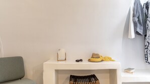 A minimalist room with a white console table, a grey sofa, and a small wooden stool. - Santo Bloom Luxury Villas with Sea View & Two Pools (Santorini)