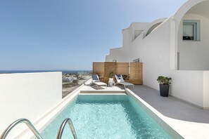 A rooftop pool with two sun loungers and a potted plant, overlooking a cityscape.