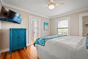 A bedroom with a bed, a ceiling fan, a TV mounted on the wall, and a window with blinds.