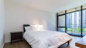 Una camera da letto moderna con un letto grande, un comodino e vista sulla città attraverso ampie finestre.