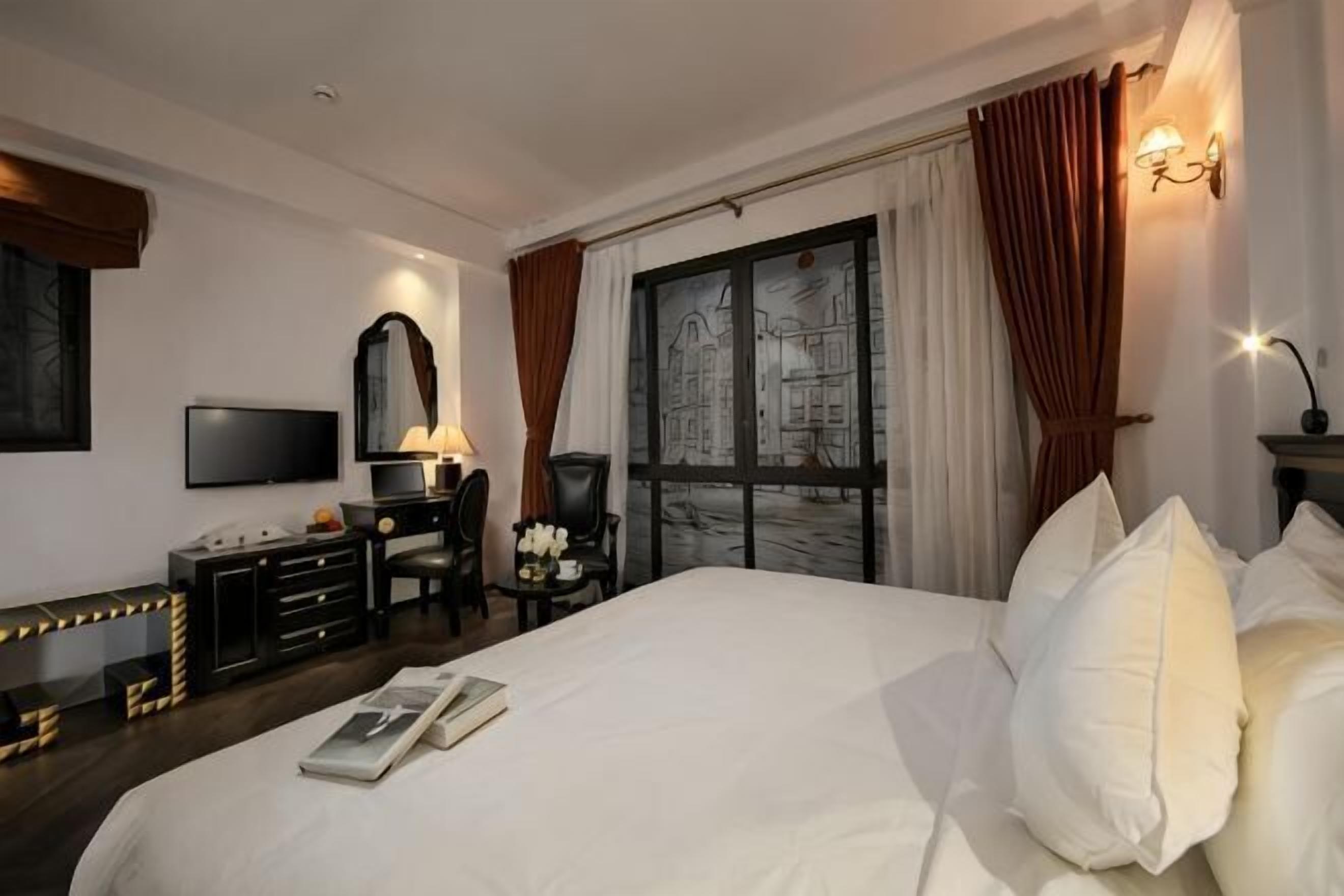 A hotel room with a large bed, a desk with a chair, a TV, and a window with curtains.