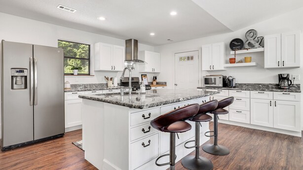 Una cocina moderna con armarios blancos, un refrigerador de acero inoxidable, una encimera de mármol y taburetes de bar.