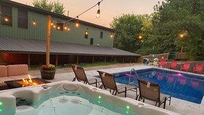 Un jacuzzi con luces LED, una piscina, mobiliario exterior y un edificio al fondo.
