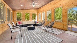 Una habitación amplia con un sofá seccional grande, una mesa de centro y sillones mecedores. La habitación cuenta con ventanas amplias y un ventilador de techo.