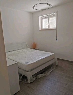 A bedroom with a bed, a nightstand, a lamp, and a window.