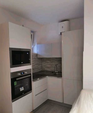 A compact kitchen with built-in appliances, including a microwave, oven, and refrigerator, and a small countertop with a sink.